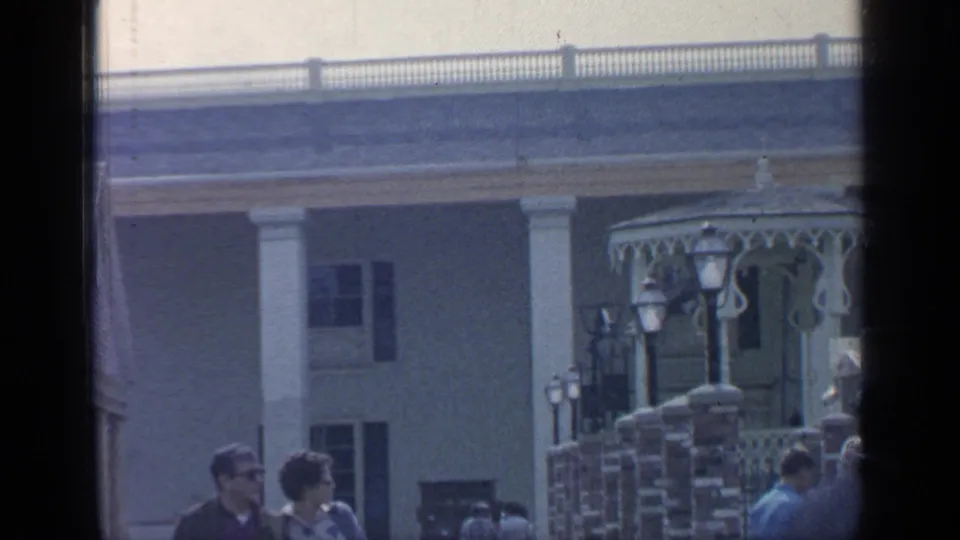 End of the 1964 Flushing Meadows pan with a columned facade, decorative gazebo structure, lampposts, brick posts, and visitors below.
