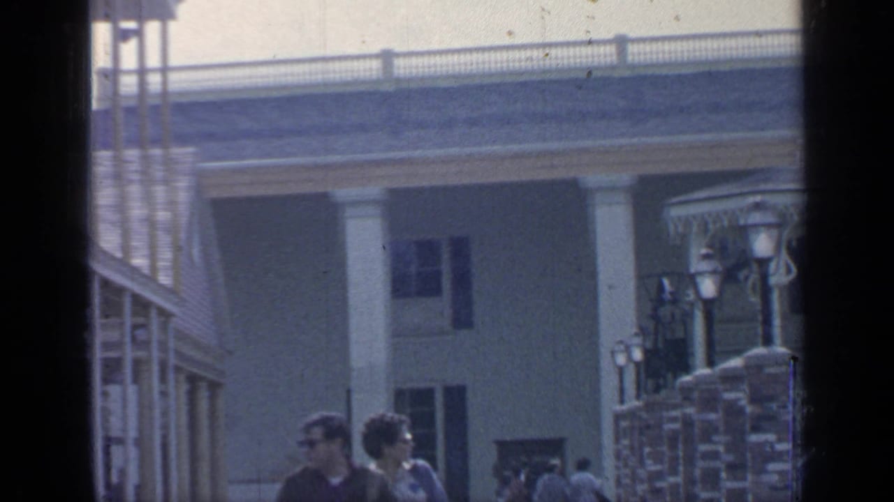 1964 Flushing Meadows visitors pass a mid-century exhibition building with columns, railings, and lampposts.