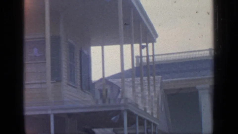 Handheld 8mm view of fairground architecture with vertical posts, railing, and sunlit wall detail.