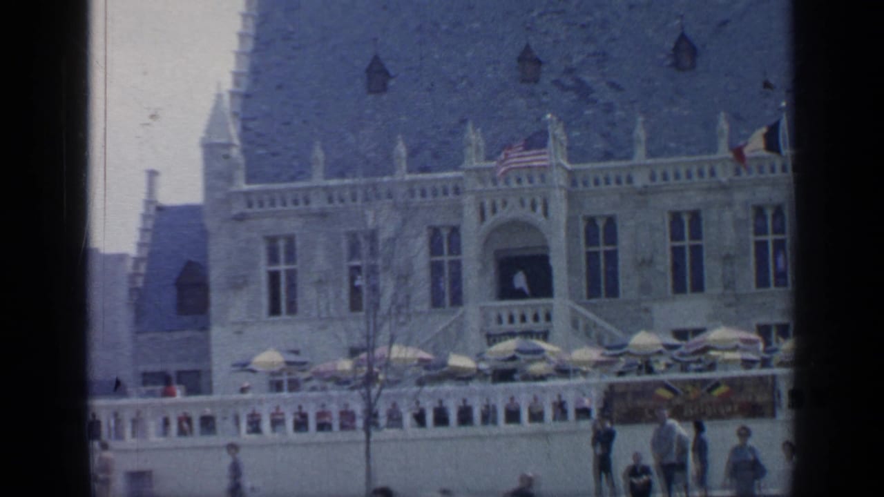 Ornate building with American and French flags, umbrellas, and pedestrians in front.