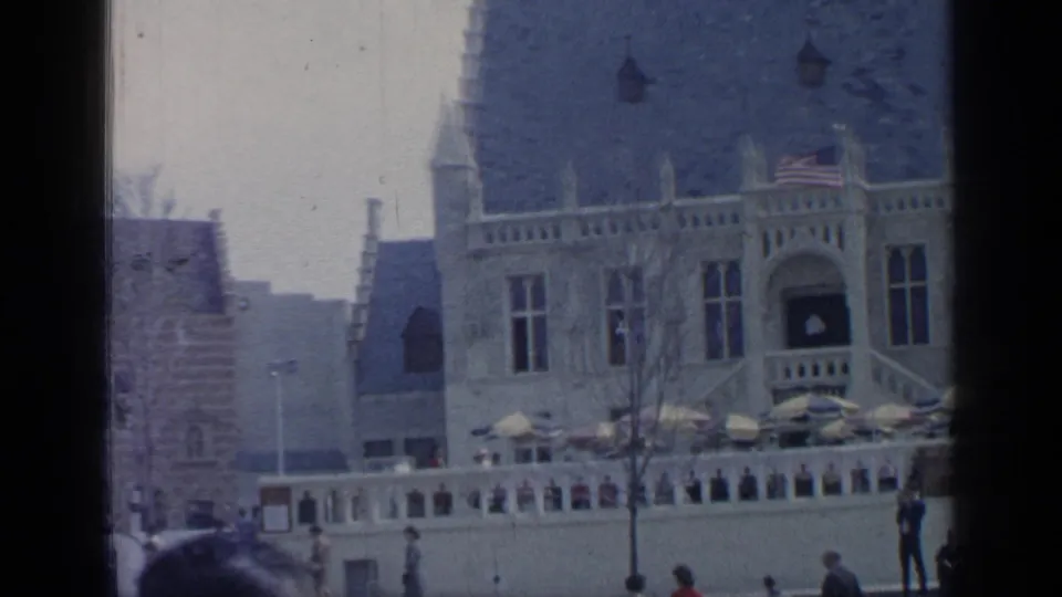 1964 Flushing Meadows exterior view with flags above a formal building and visitors moving near a terrace wall.