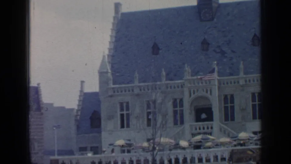 Visitor-shot 1964 Flushing Meadows frame of a blue-roofed ornate building with flags and terrace umbrellas.