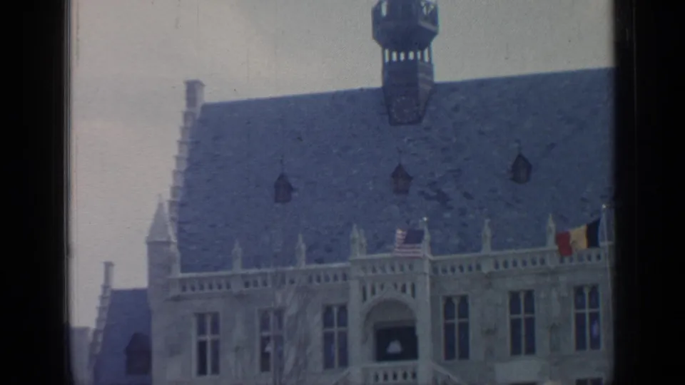 1964 Flushing Meadows frame showing the roofline, flags, ornate windows, and balcony of a fairground building.