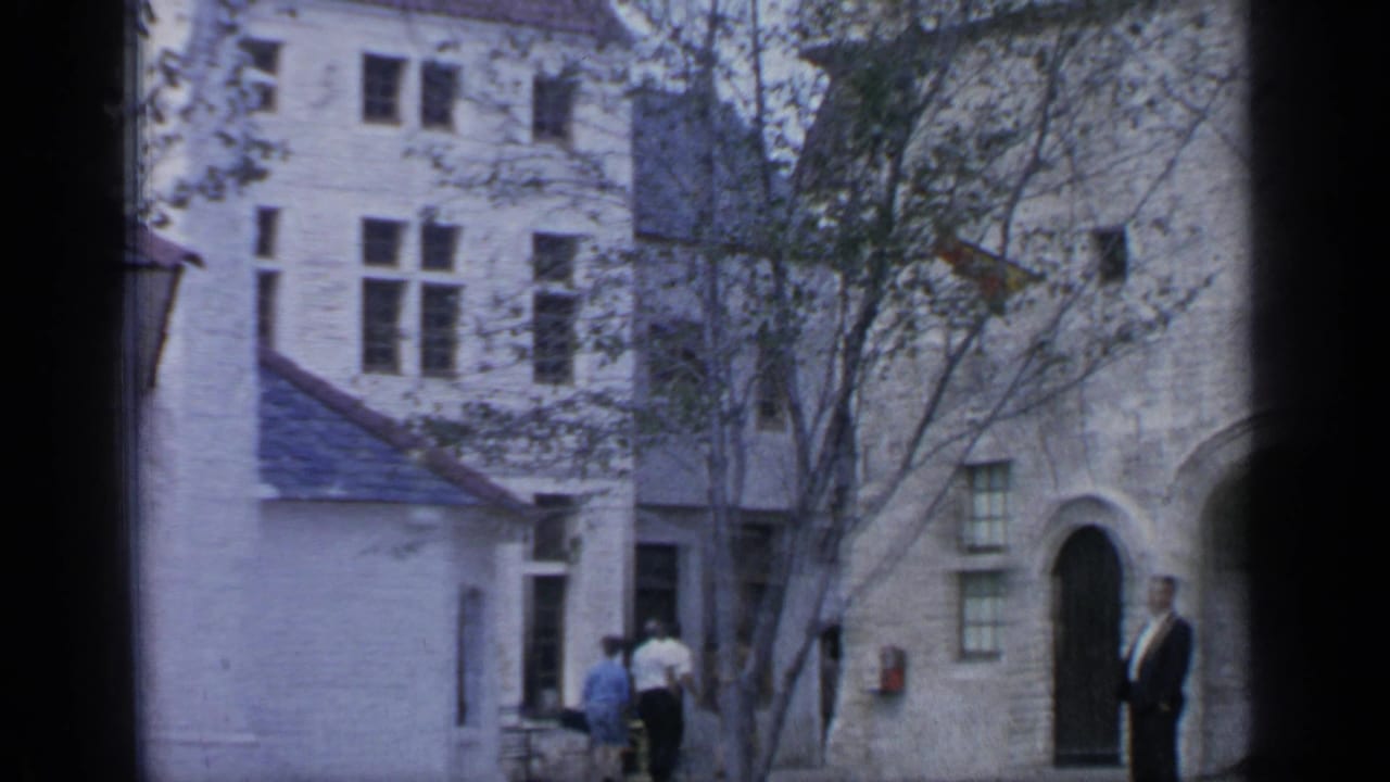Visitors near pale stone buildings with arched doors and trees in a courtyard.