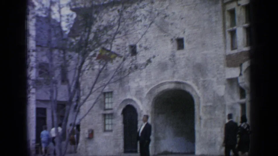 1964 Flushing Meadows frame with a man in a dark suit near an arched stone entrance and visitors moving behind him.