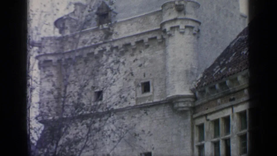 1964 Flushing Meadows frame showing a crenellated pale stone wall, tower-like corner detail, windows, and trees in the foreground.