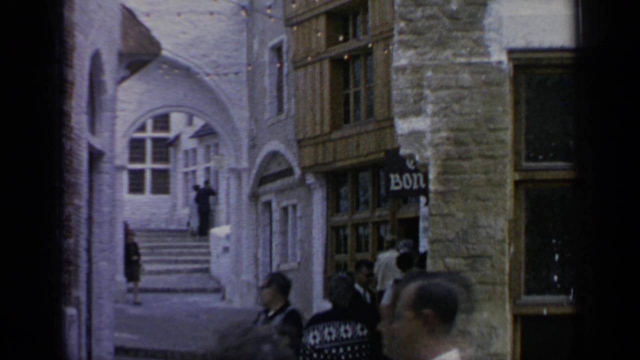 Visitors move through a narrow themed village walkway at Flushing Meadows, with arched windows, stonework, timber trim, and visible signage.