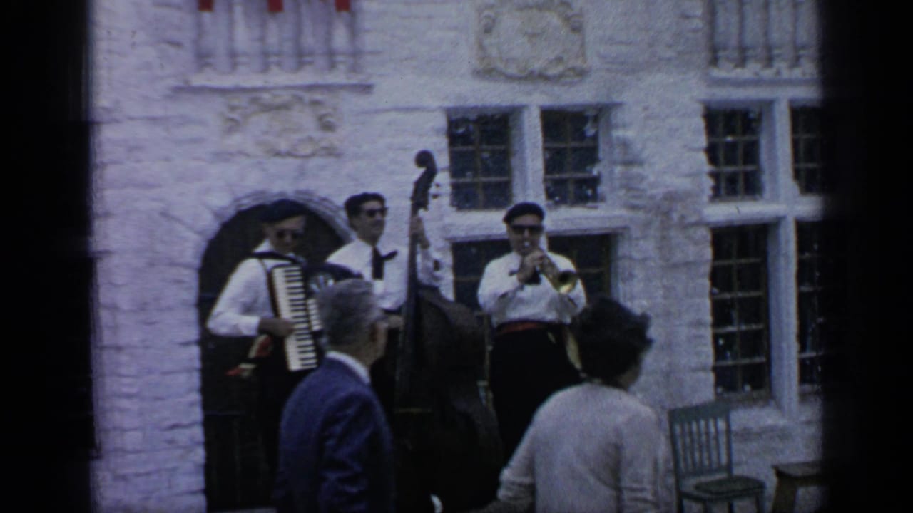 Three musicians perform outside a white stone building while visitors watch.