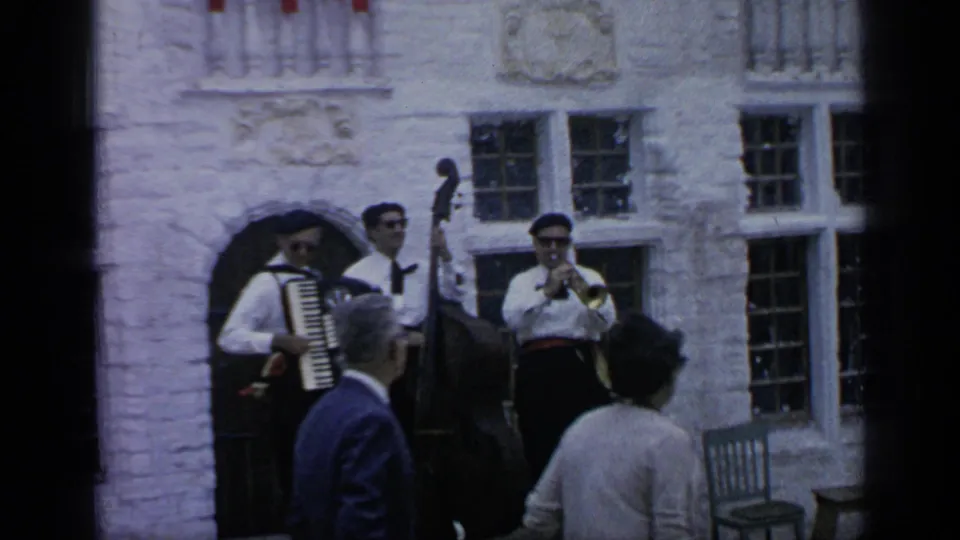 1964 Flushing Meadows frame showing period-costumed street musicians with accordion, upright bass, and horn before a white stone facade.