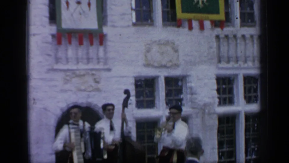 1964 Flushing Meadows home-movie frame of musicians performing beneath colorful banners on a historic-style facade.
