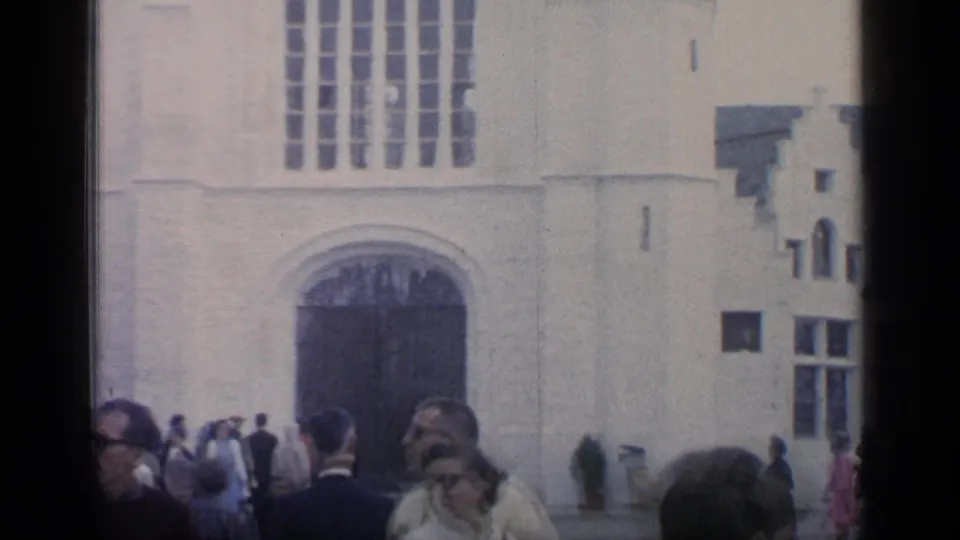 1964 Flushing Meadows 8mm frame showing visitors near the dark entrance of a white Gothic-style facade with tall arched windows.