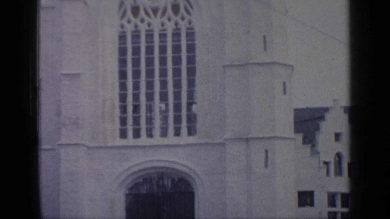 White facade with a tall arched window and dark entrance below.