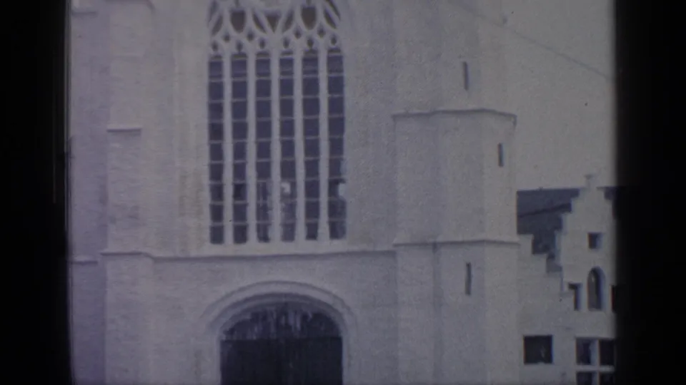 1964 Flushing Meadows frame focused on the white building facade, tall Gothic-style window, and dark arched doorway.