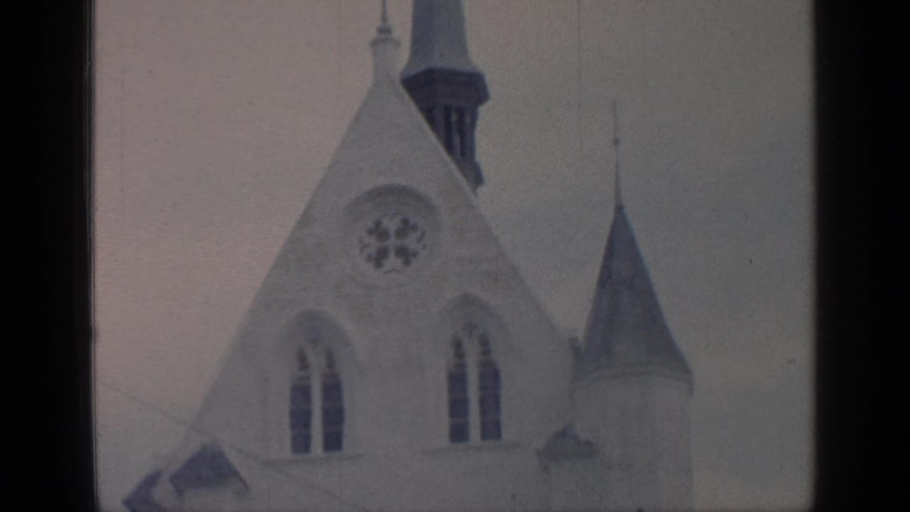 Pale church roofline with rose window, arched windows, spire, and cross.