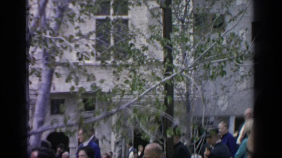 1964 Flushing Meadows fair visitors move through a tree-lined area, with buildings and dark frame edges visible.