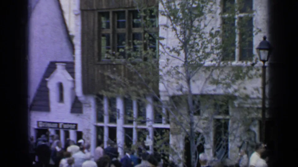 World's Fair visitors cluster below a timbered facade and small gabled entrance, with trees and a street lamp nearby.