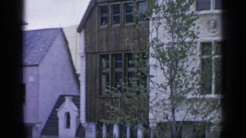 A handheld view settles on a fair building facade with timbered upper windows, trees, and a pale gabled roof in Flushing Meadows.