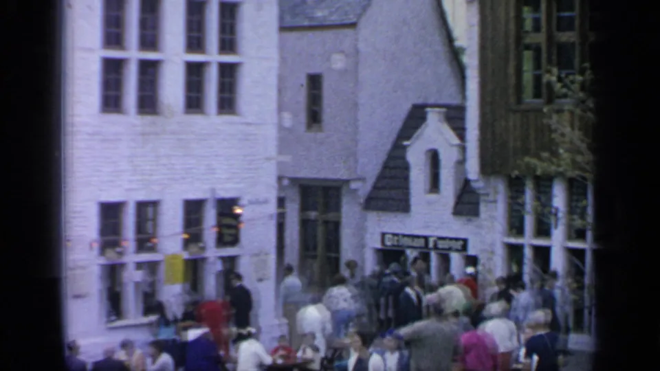 1964 Flushing Meadows fairgoers move through a European-style village street with a visible Belgian Fudge storefront sign.