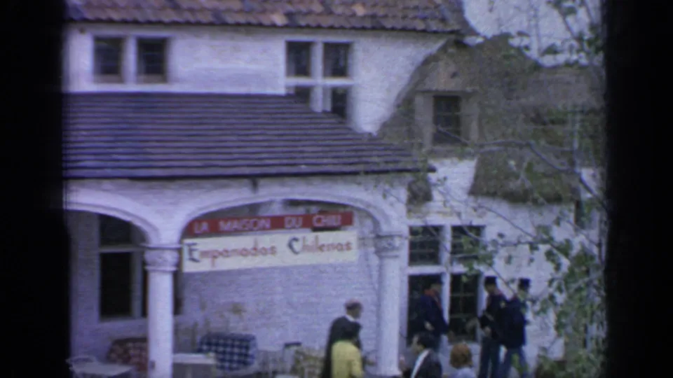 1964 Flushing Meadows footage shows La Maison du Chili and Empanadas Chilenas signage above pedestrians near a white exhibit facade.