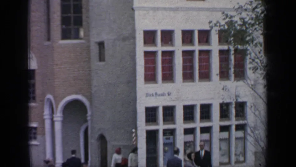 1964 Flushing Meadows street-level view with pedestrians, an arched doorway, a pale facade and red-tinted window panels.