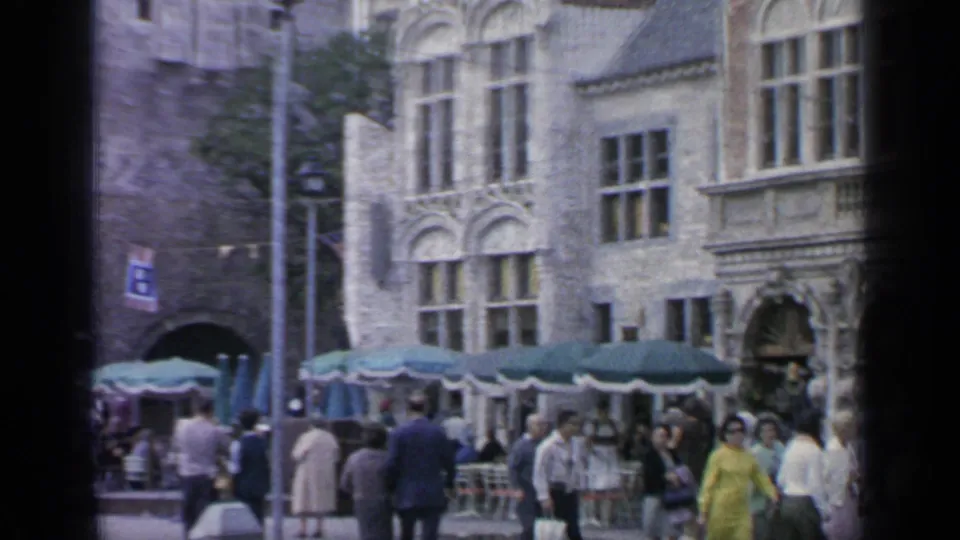 1964 Flushing Meadows public scene with pedestrians, green outdoor umbrellas, ornate stone facades and an arched passage in the background.