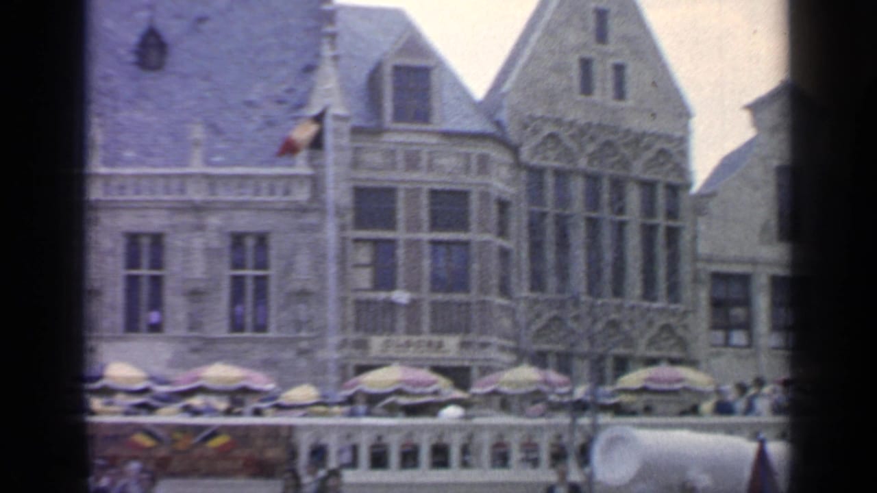 1964 Flushing Meadows fairground view with Gothic-style facades, outdoor umbrellas, and visitors gathered along the plaza.