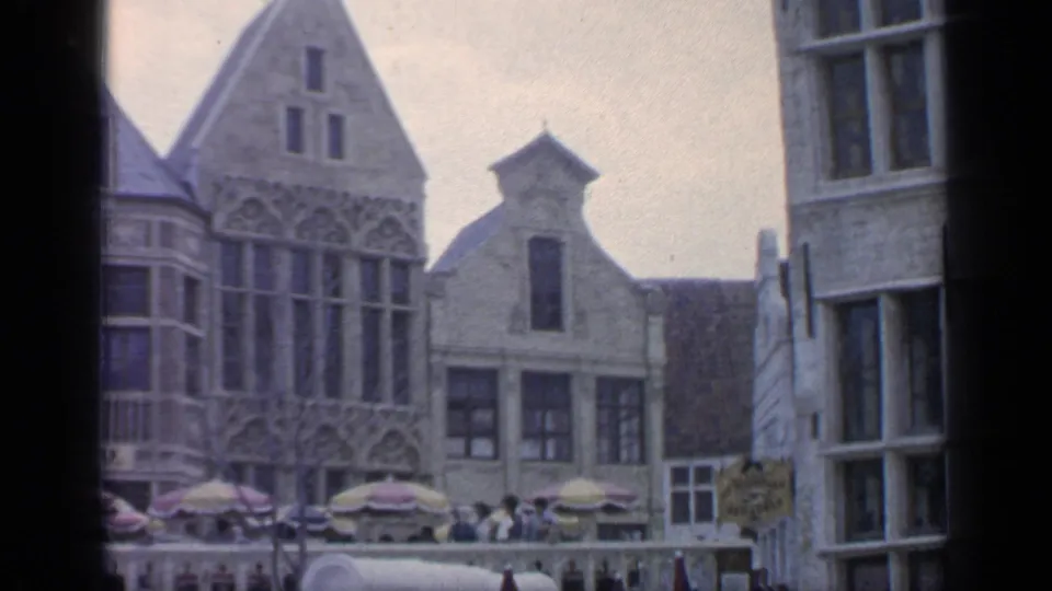 Handheld 8mm view of 1964 Flushing Meadows fair architecture, with tall gables, windows, umbrellas, and visitors below.
