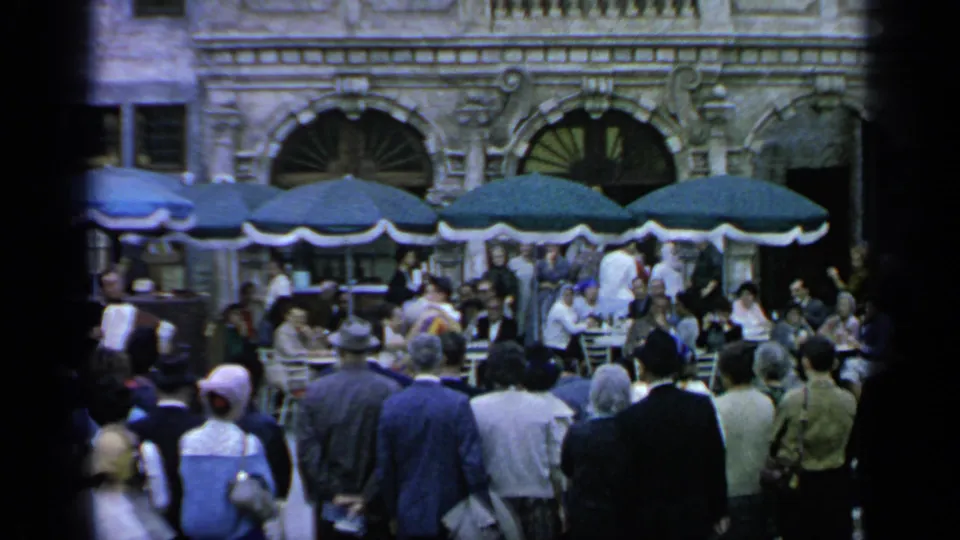 1964 Flushing Meadows crowd scene with visitors gathered before cafe umbrellas and an ornate building with arched windows.
