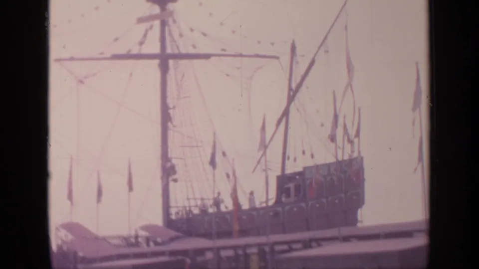 1964 Flushing Meadows frame of the moored display vessel with tall rigging, small flags, and distant visitors on deck.