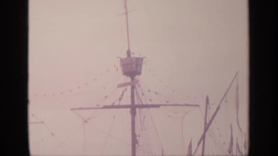 Faded 8mm frame from Flushing Meadows showing the ship model's central mast, crow's nest, rigging, and nearby flagpole.
