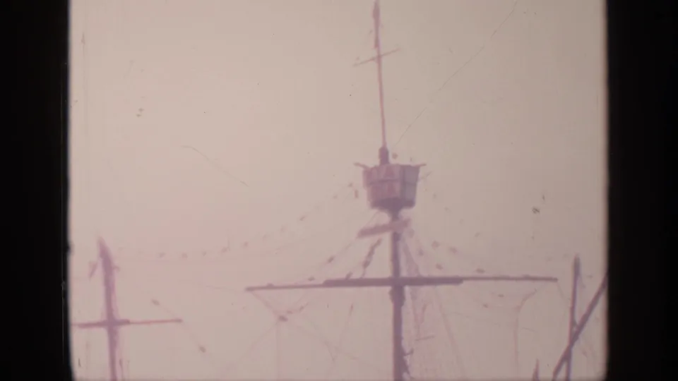 Soft 1964 8mm view of a ship model mast and crow's nest at the World's Fair, with rigging and flags fading into the pale sky.