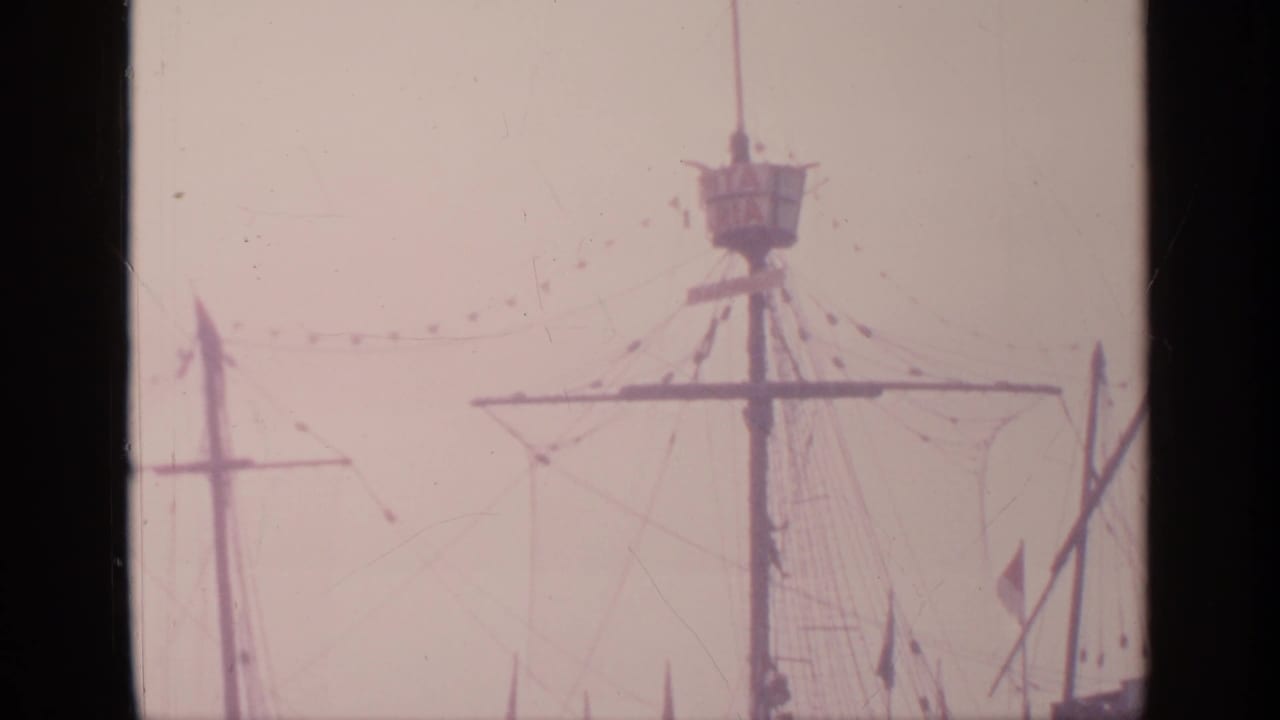 Tall ship mast and rigging against a pale hazy sky.