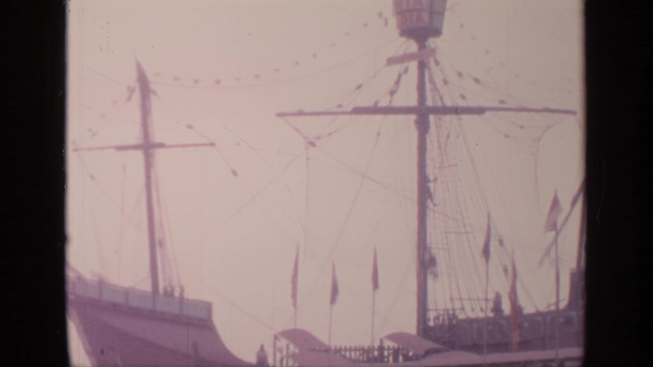 Ship bow, mast, rigging, and flags seen above a fairground structure.