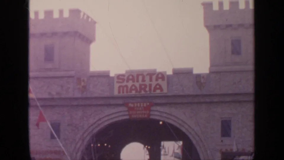 1964 Flushing Meadows frame showing a castle-like Santa Maria entrance with towers, sign, arch, and distant visitors.