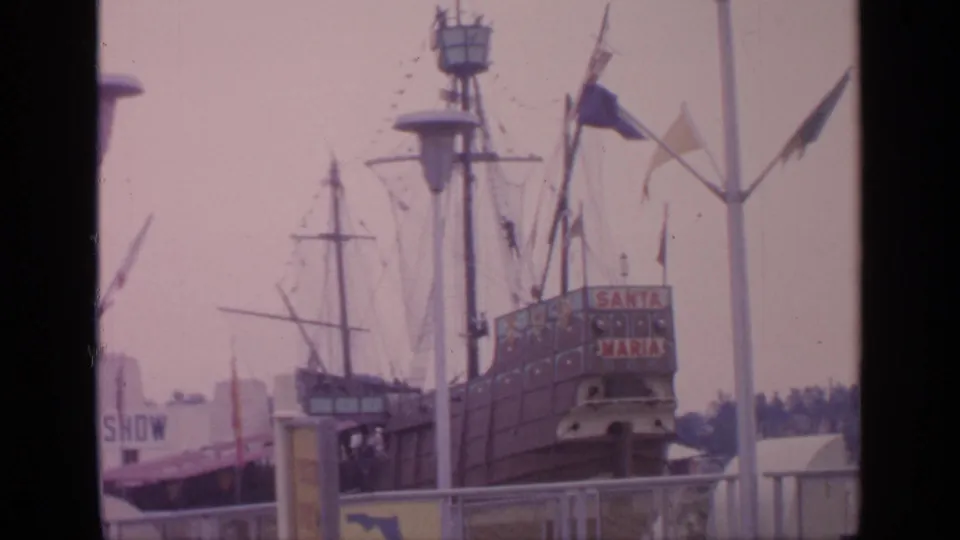 1964 Flushing Meadows World's Fair view of the Santa Maria replica with flags, signage, masts, and visitors near the attraction.