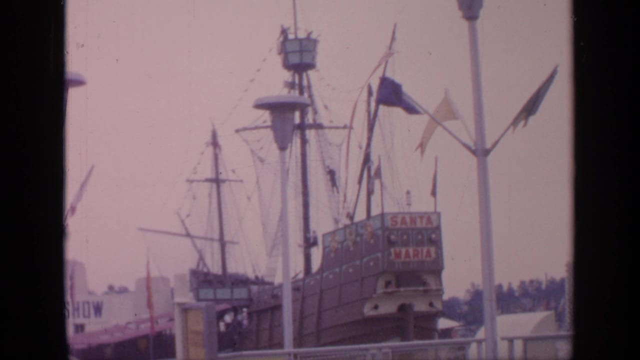 1964 Flushing Meadows World's Fair frame showing the Santa Maria replica, fairground railings, flags, and visitors near the ship attraction.
