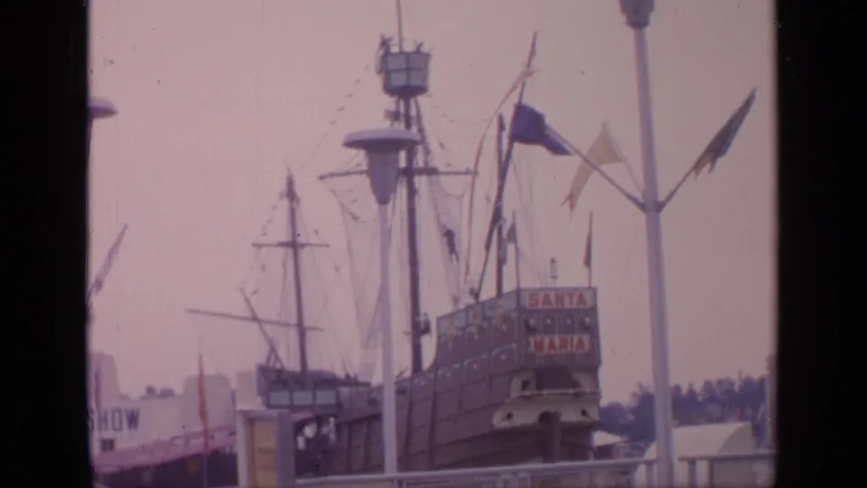 1964 Flushing Meadows World's Fair frame showing the Santa Maria replica, fairground railings, flags, and visitors near the ship attraction.
