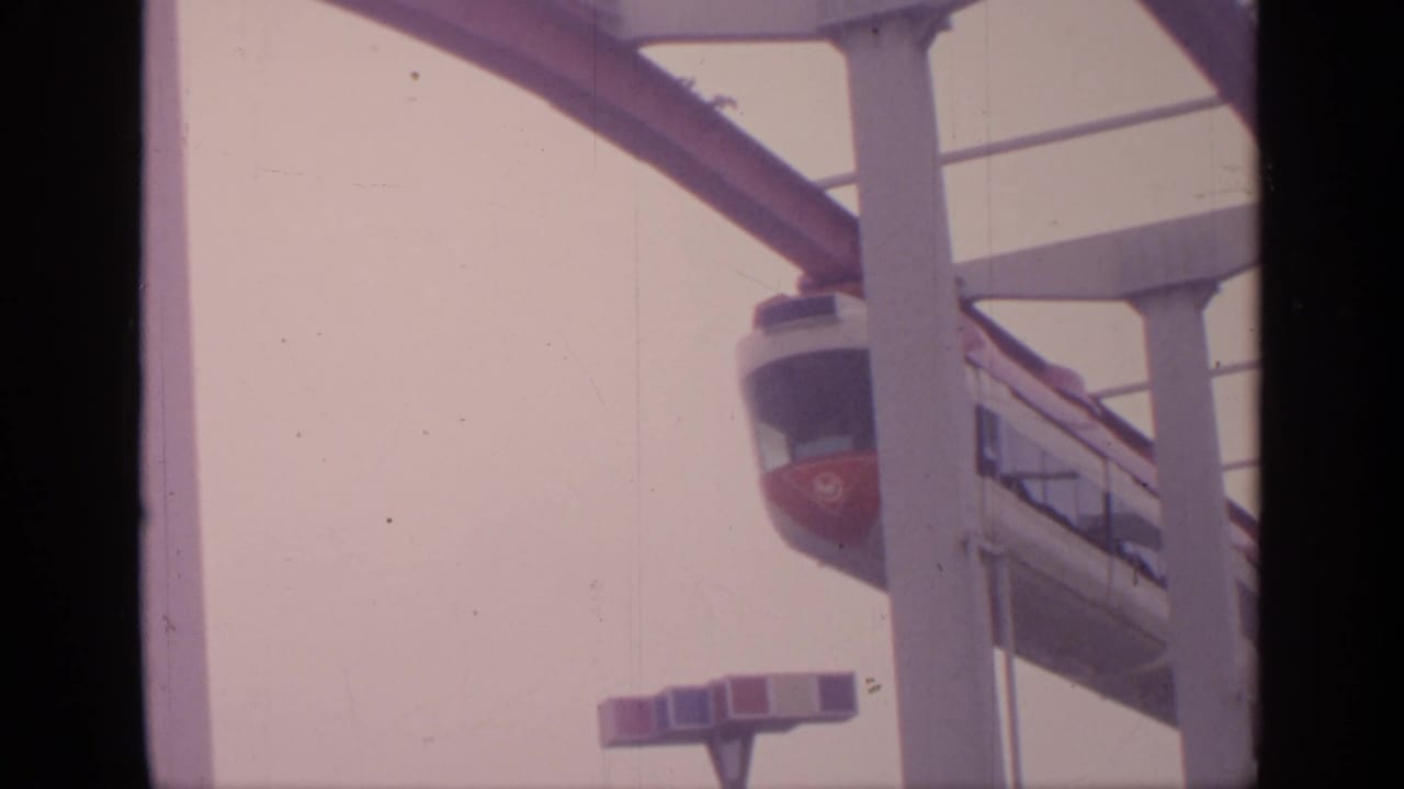 Red-and-white aerial tramway car moving along an elevated track against a pale sky.