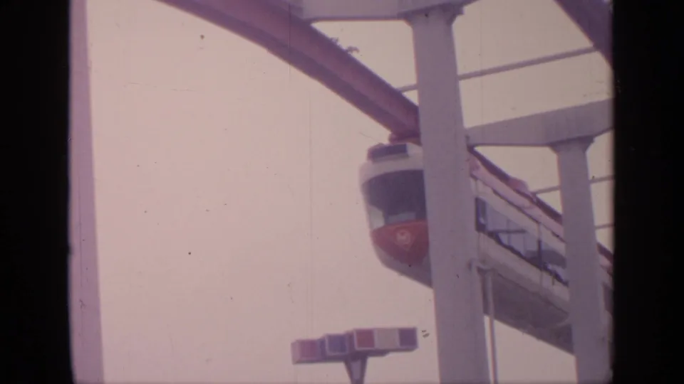 1964 Flushing Meadows frame of a red-and-white tramway car on an elevated guideway with white support columns.