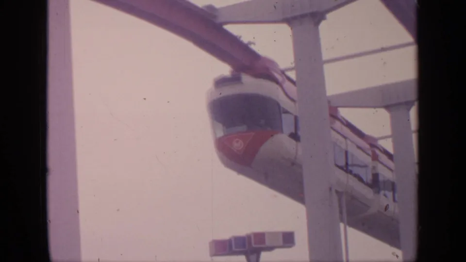 Close 1964 Flushing Meadows view of the red-and-white tramway car passing under the elevated rail structure.
