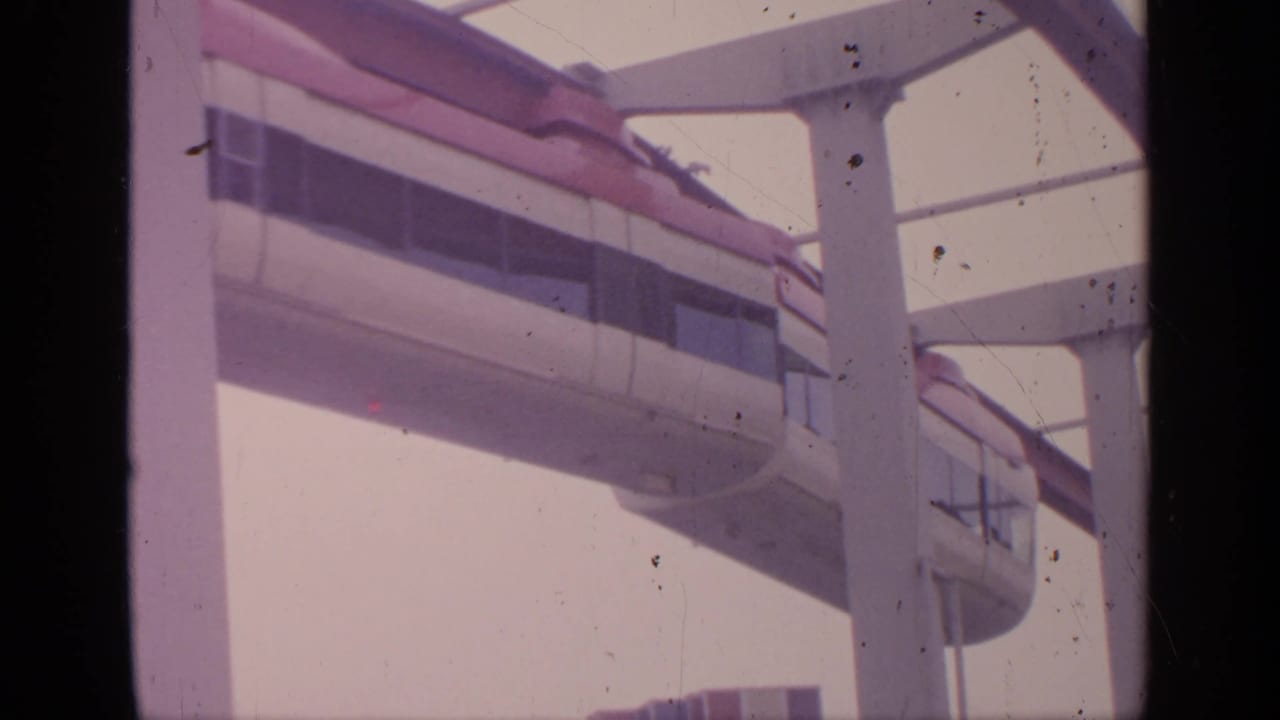 Side of monorail car moving along elevated track behind white columns.