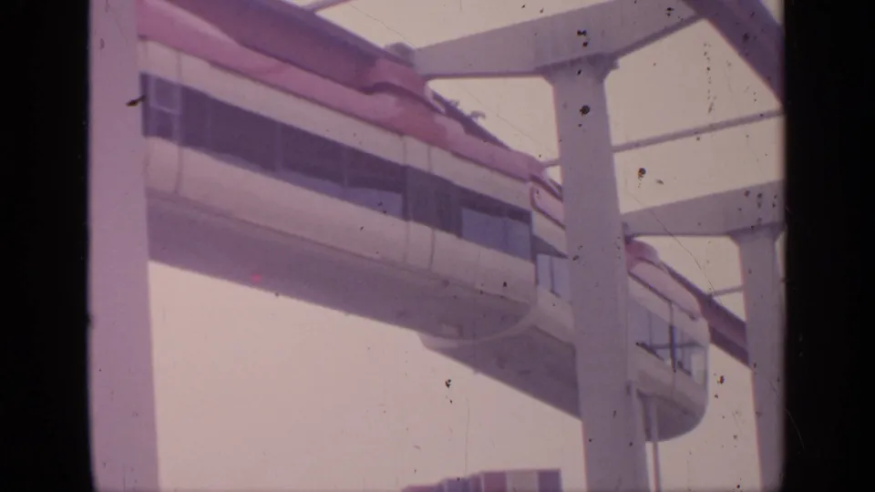 White monorail car with dark windows travels right to left along a red elevated rail at Flushing Meadows in 1964.