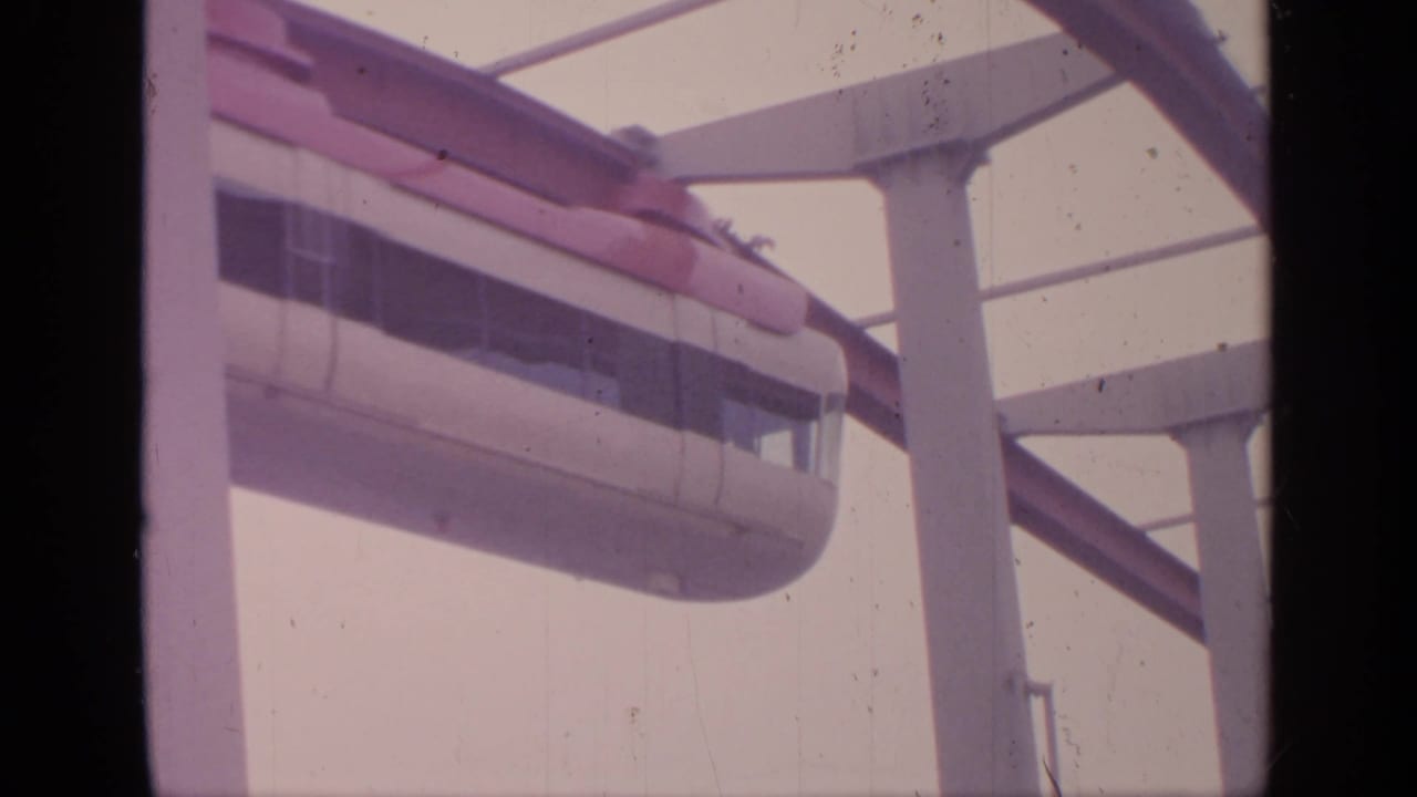 Red-and-white monorail car passing on an elevated track near support columns.