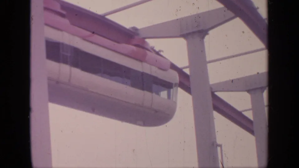 1964 Flushing Meadows 8mm frame showing a red-and-white monorail moving along an elevated guideway beside modern supports.