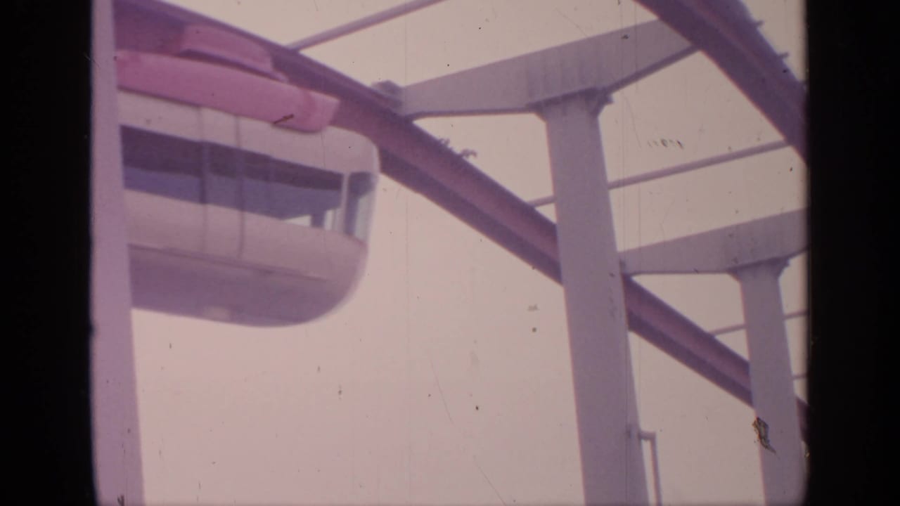 Monorail car partly framed under the elevated red track and concrete supports.