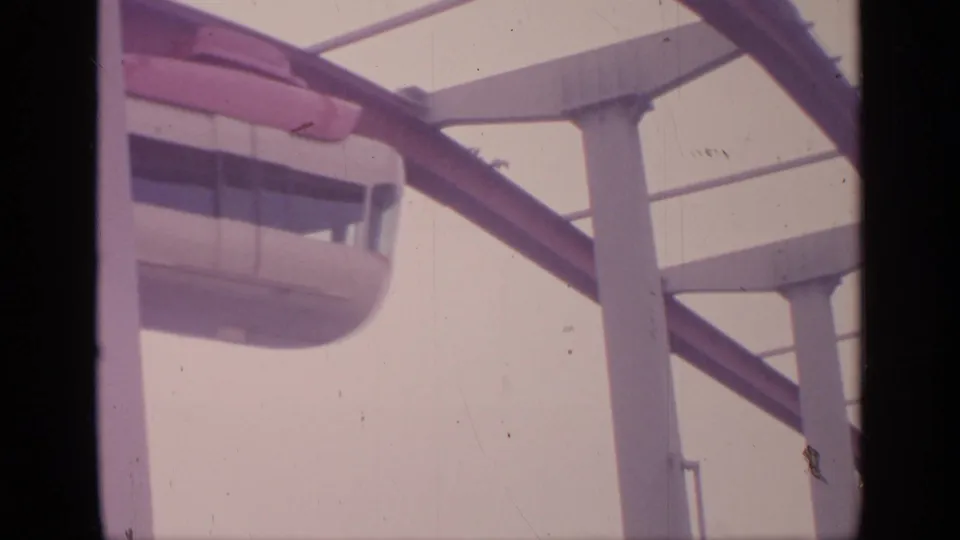 The monorail appears close to the camera beneath red guideway rails and pale structural supports at Flushing Meadows in 1964.