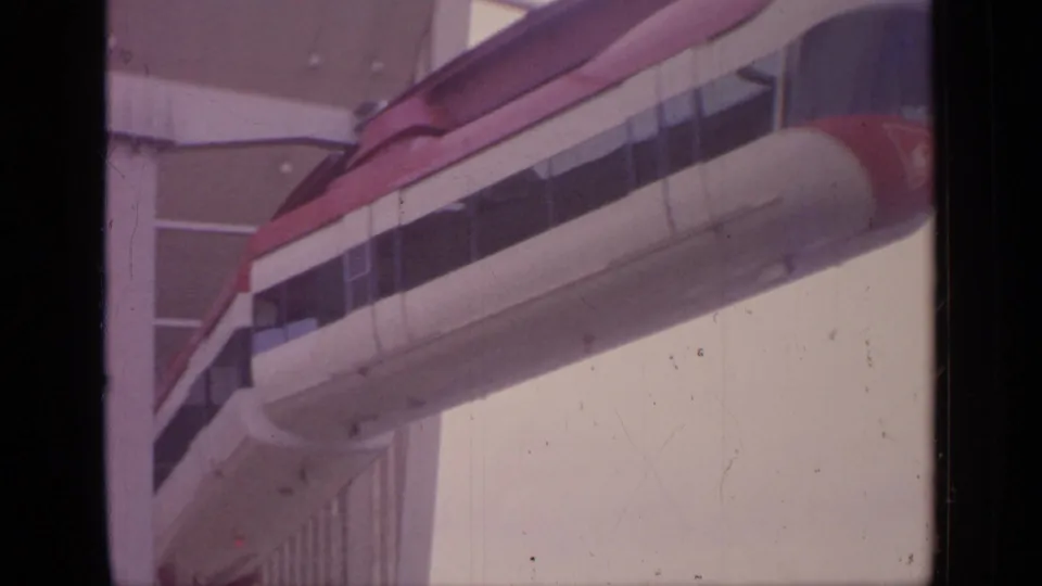 Close 1964 Flushing Meadows view of the monorail car alongside the elevated guideway, with building windows visible behind it.