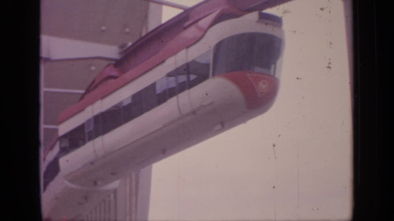 Red-and-white monorail entering an elevated station beside large windows.