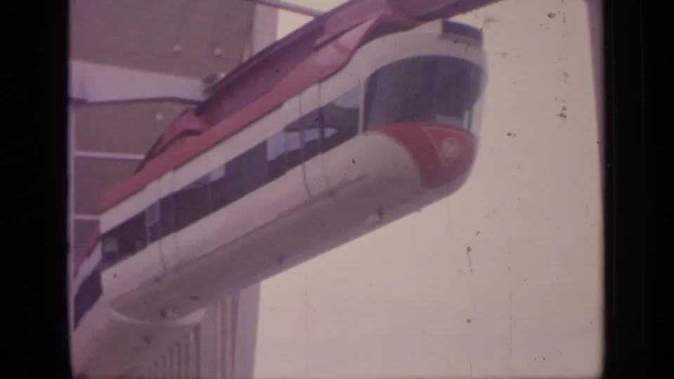 1964 Flushing Meadows home-movie frame showing a red-and-white monorail approaching a multi-windowed elevated station.