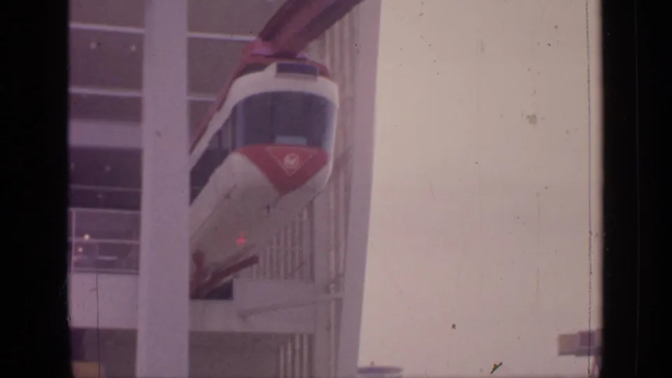 Visitor-shot 8mm frame of the monorail moving deeper into the multi-windowed station at Flushing Meadows.
